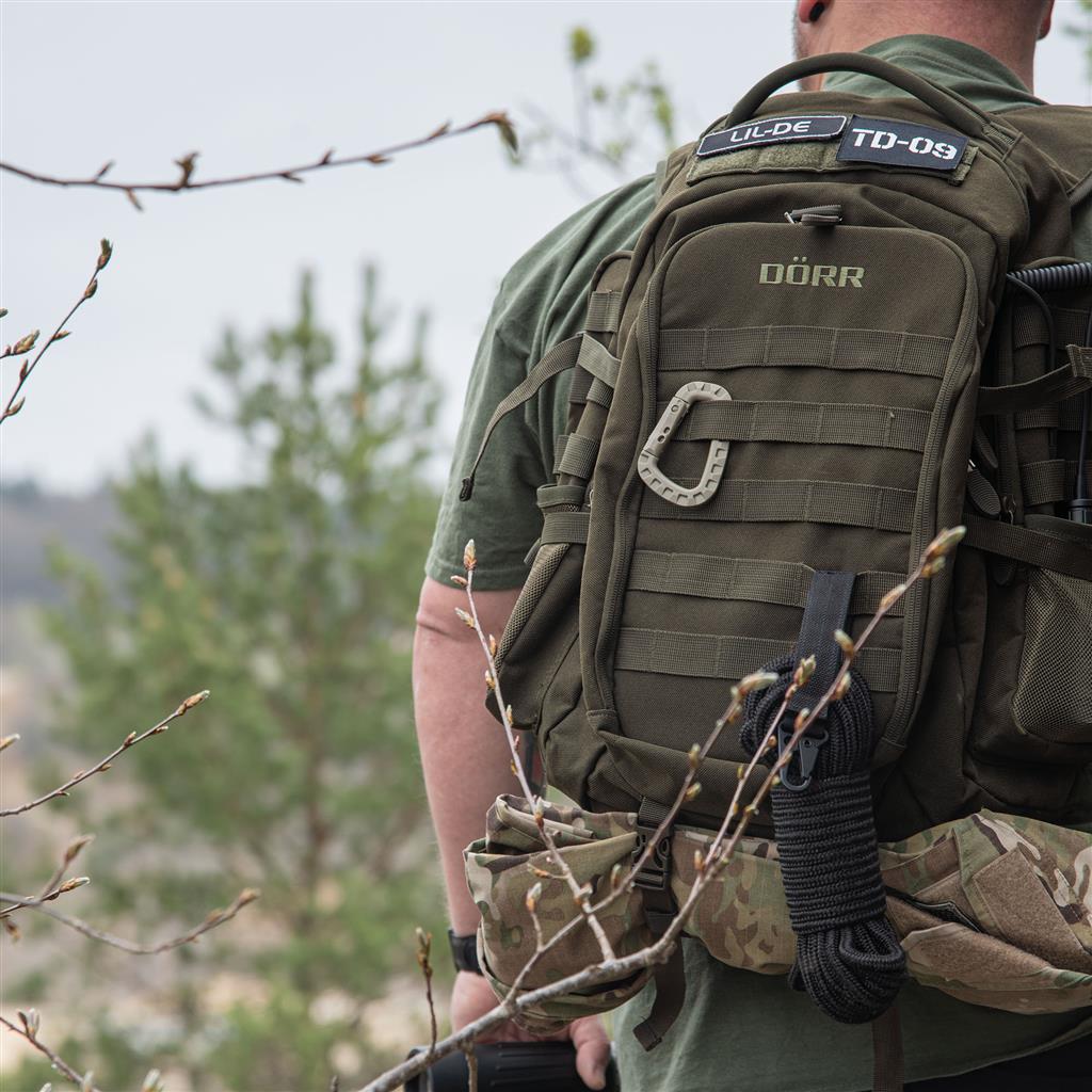 DÖRR ProTac taktischer Outdoor-Rucksack oliv mit MOLLE-System, getragen im Outdoor-Einsatz mit Patches und Zubehör