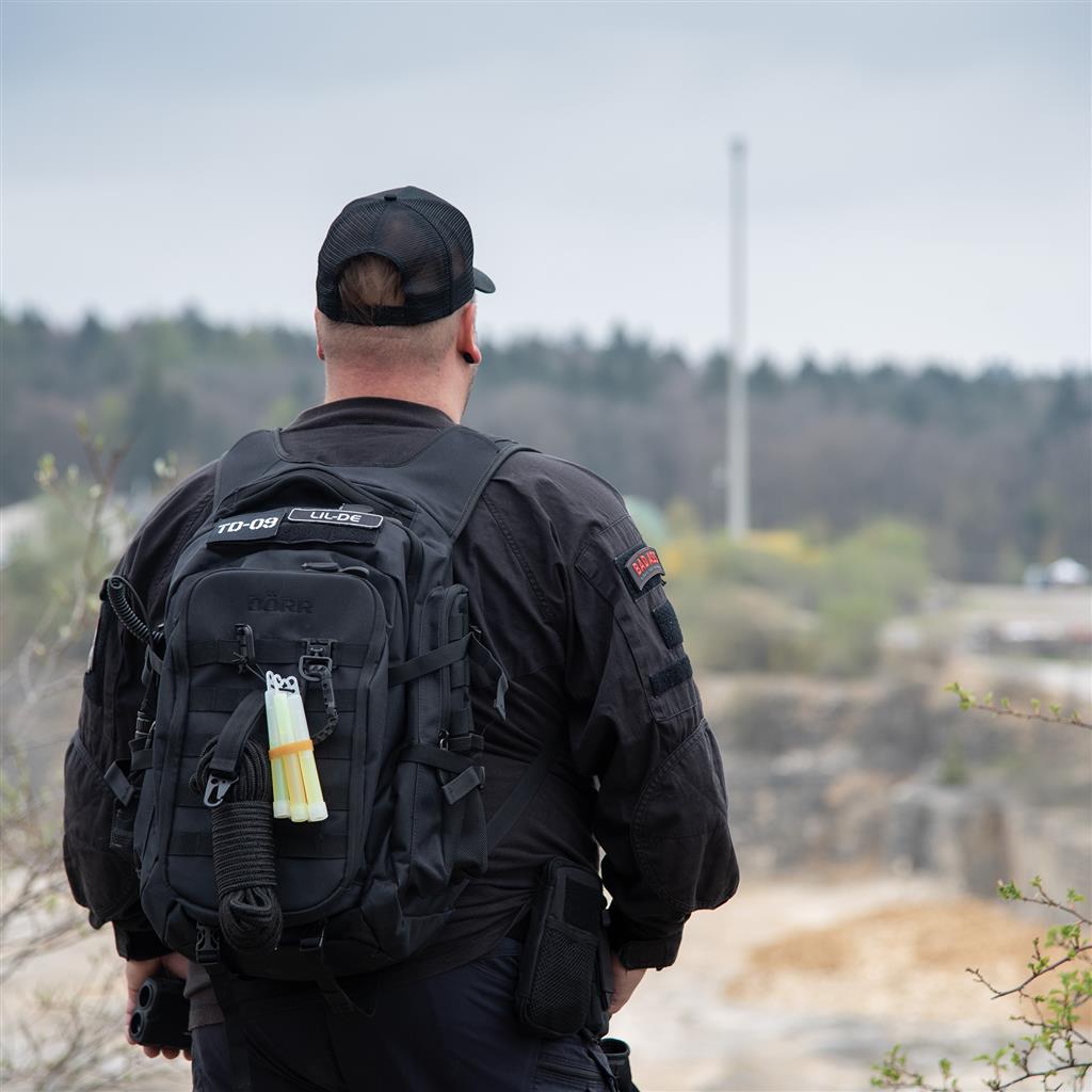 DÖRR ProTac taktischer Outdoor-Rucksack schwarz mit MOLLE-System, getragen im Outdoor-Einsatz mit Patches und Zubehör